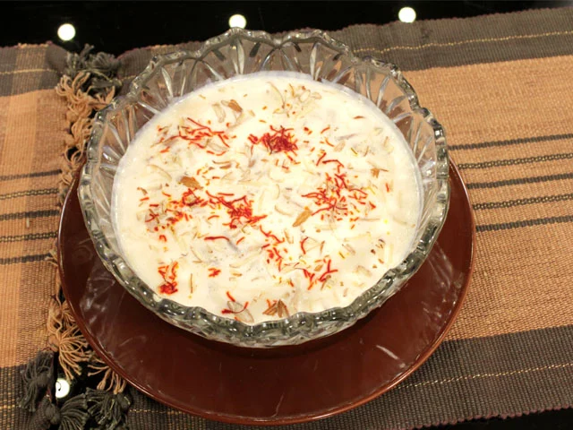 A bowl of saffron kheer, a traditional rice pudding, garnished with nuts, placed on a table.